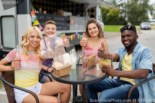 Image of happy friends with drinks eating at food truck