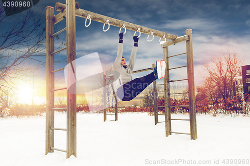 Image of young man exercising on horizontal bar in winter