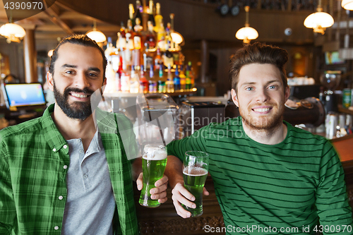 Image of male friends drinking green beer at bar or pub