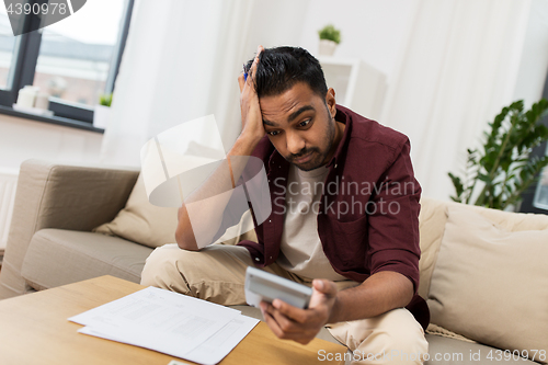 Image of confused man with papers and calculator at home