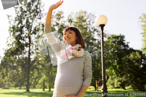 Image of happy pregnant asian woman waving hand at park