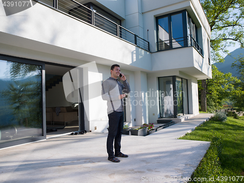 Image of man using mobile phone in front of his luxury home villa