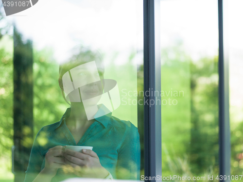 Image of young woman drinking morning coffee by the window