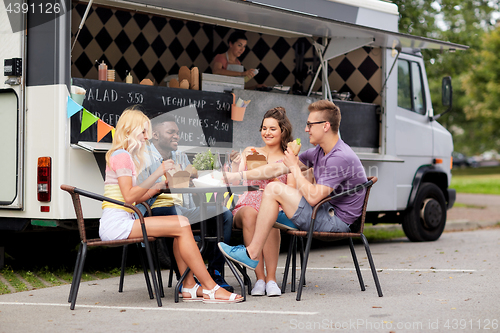 Image of happy friends with drinks eating at food truck