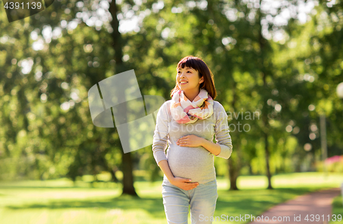 Image of happy pregnant asian woman walking at park