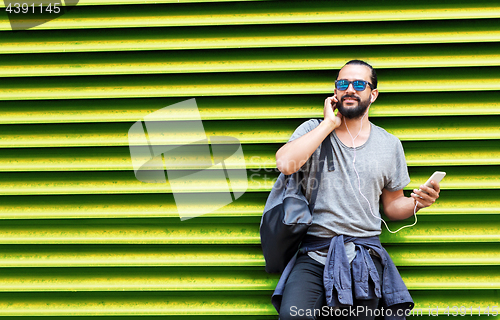Image of man with earphones and smartphone over wall