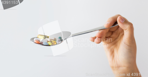 Image of close up of female hand holding spoon with pills