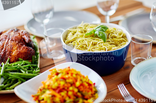 Image of pasta with basil in bowl and other food on table