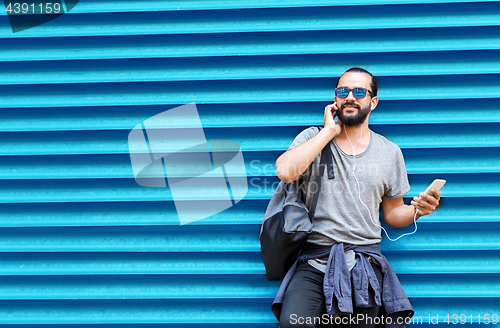 Image of man with earphones and smartphone over wall