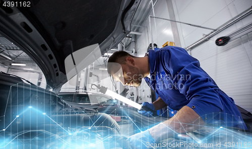 Image of mechanic man with lamp repairing car at workshop