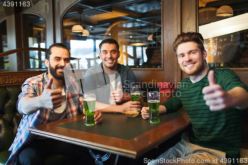 Image of male friends drinking green beer at bar or pub