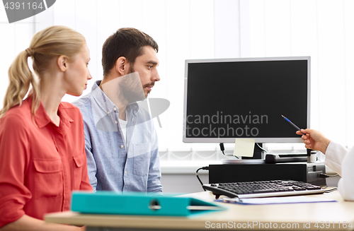 Image of couple and doctor pointing at computer at clinic