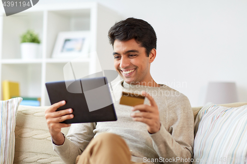 Image of smiling man with tablet pc and credit card at home