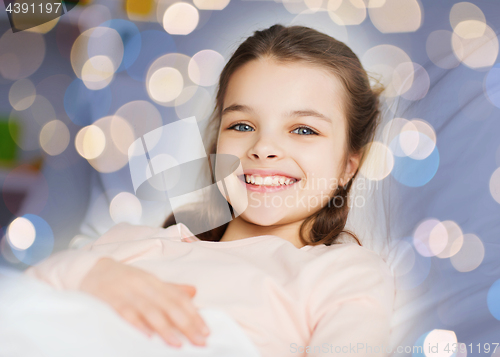 Image of happy smiling girl lying awake in bed over lights