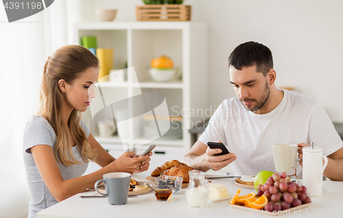 Image of couple with smartphones having breakfast at home