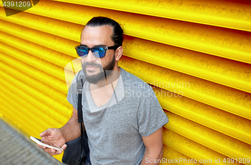 Image of man in sunglasses with smartphone and bag at wall