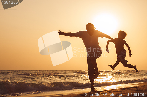 Image of Father and son  playing on the beach at the sunset time.