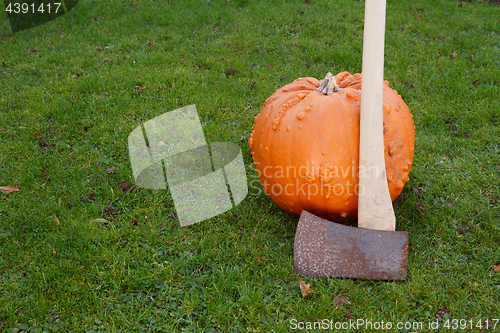 Image of Axe leans against large orange pumpkin
