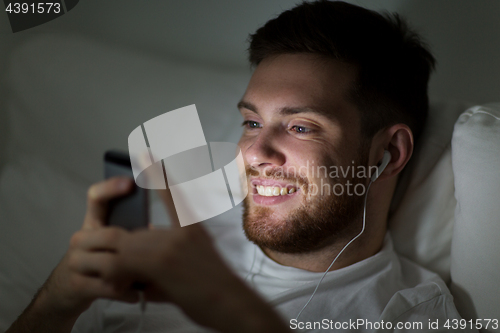Image of man with smartphone and earphones in bed at night