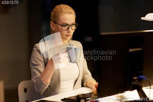 Image of businesswoman at night office drinking coffee