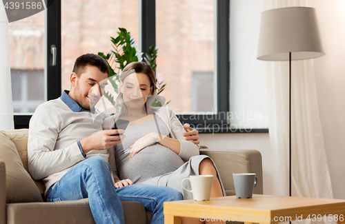 Image of man and pregnant wife with smartphone at home