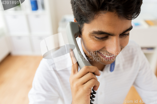 Image of happy businessman calling on desk phone at office