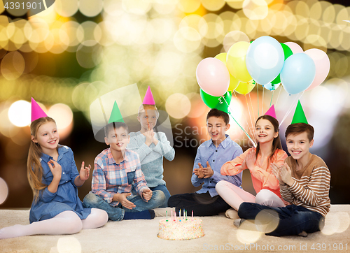 Image of happy children in party hats with birthday cake