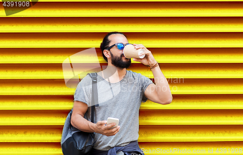 Image of man with smartphone drinking coffee over wall