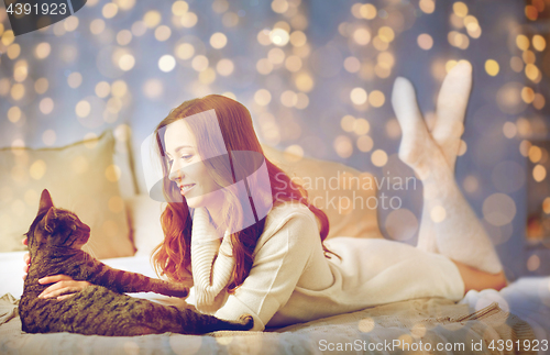 Image of happy young woman with cat lying in bed at home