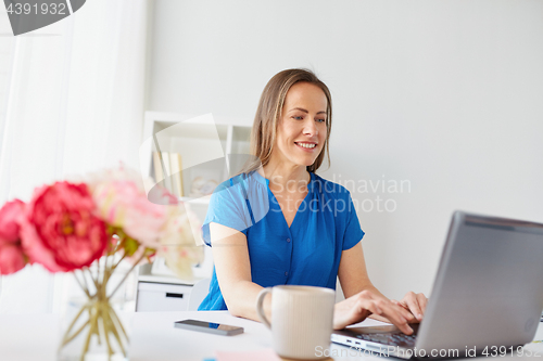 Image of happy woman with laptop working at home or office