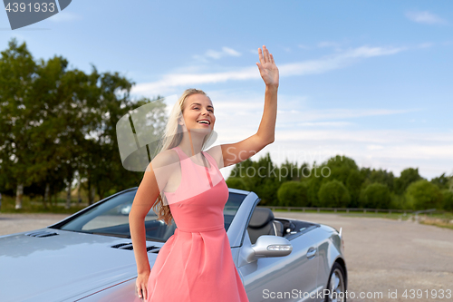 Image of happy young woman in convertible car waving hand