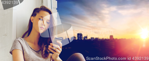 Image of sad pretty teenage girl with smartphone texting