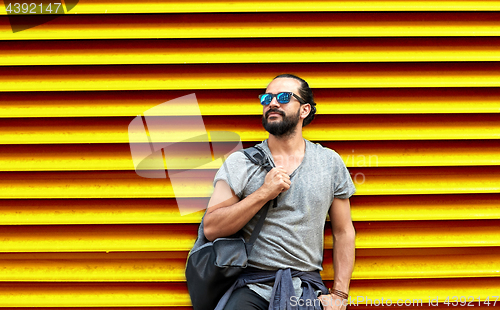 Image of man in sunglasses with bag standing at street wall