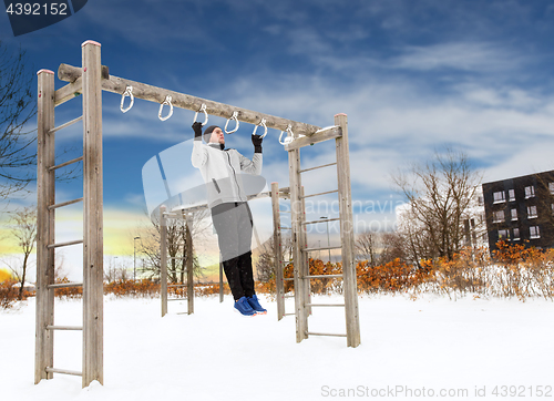 Image of young man exercising on horizontal bar in winter