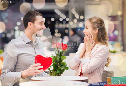 Image of happy couple with present and flowers in mall