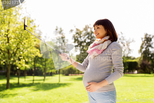 Image of happy pregnant asian woman taking selfie at park