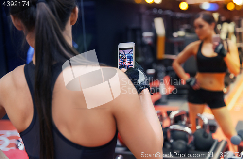 Image of woman with smartphone taking mirror selfie in gym