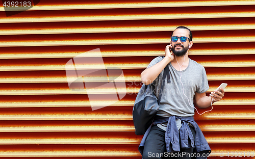 Image of man with earphones and smartphone over wall