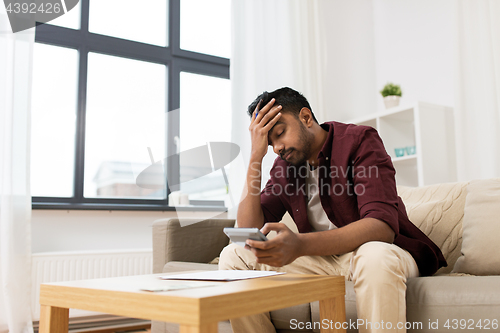 Image of upset man with papers and calculator at home