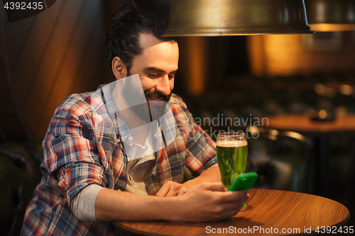 Image of man with smartphone and green beer texting at bar