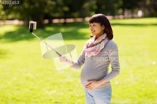 Image of happy pregnant asian woman taking selfie at park