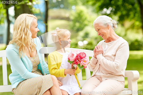 Image of happy family giving flowers to grandmother at park