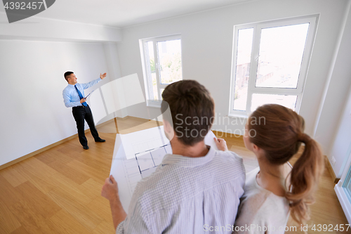 Image of realtor showing new home to couple with blueprint