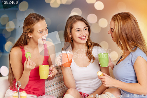 Image of happy young women drinking tea with sweets at home