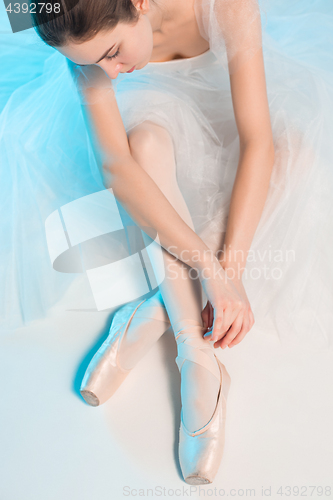 Image of Young and incredibly beautiful ballerina is sitting in a blue studio