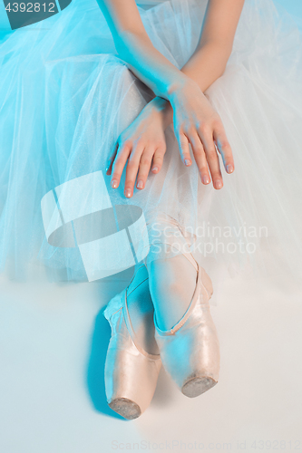 Image of Young and incredibly beautiful ballerina is sitting in a blue studio