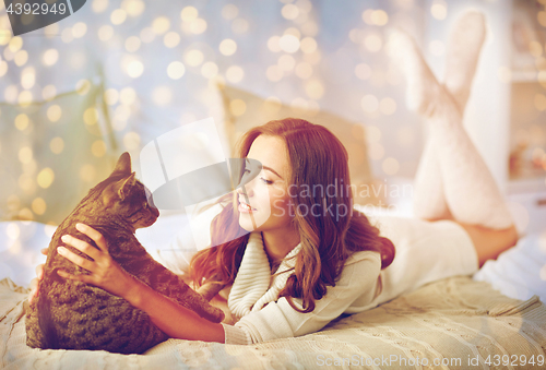 Image of happy young woman with cat lying in bed at home