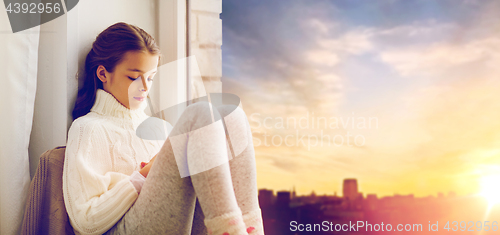 Image of sad girl sitting on sill at home window