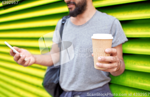 Image of man with coffee cup and smartphone over wall