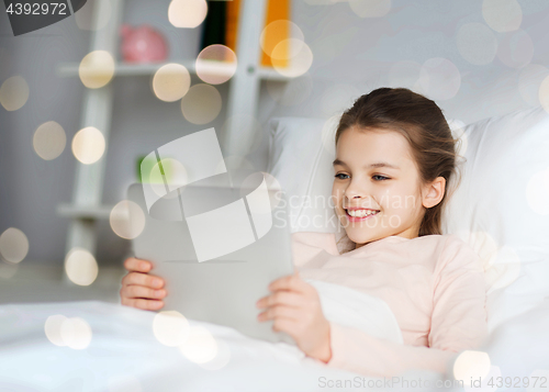 Image of happy girl lying in bed with tablet pc at home